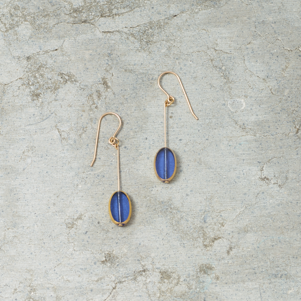 Gold earrings with blue stones on a textured gray surface