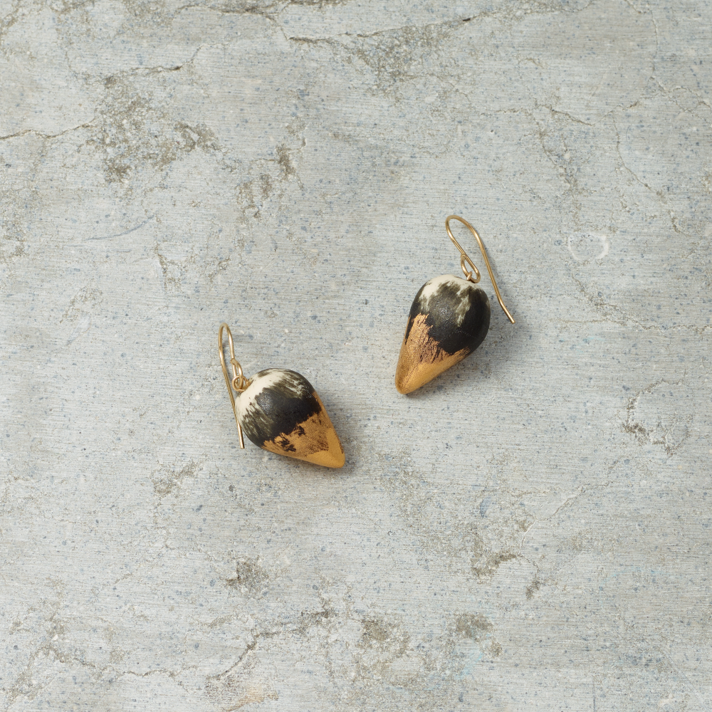 Pair of gold and black earrings on a textured gray surface