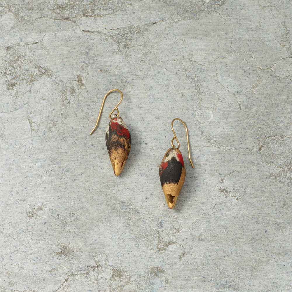 Pair of gold earrings with red and black accents on a gray stone surface