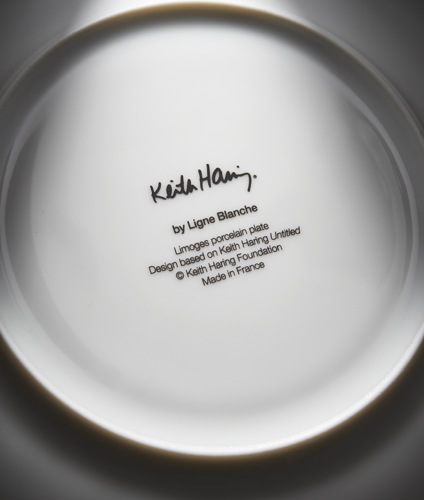 Close-up of a white plate with black text and signature, featuring 'Keith Haring' and 'Ligne Blanche'.