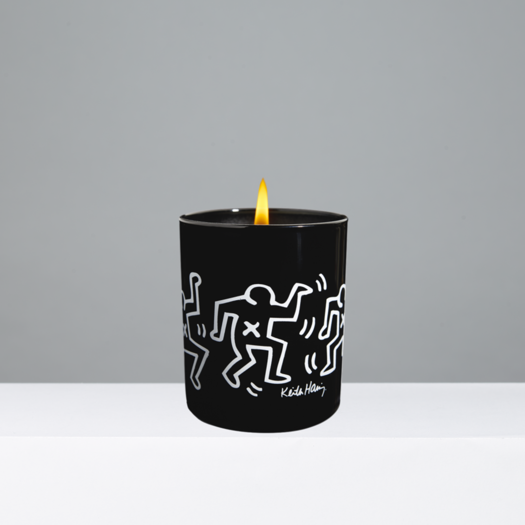 Black candle with white illustrations and a lit wick on a gray background