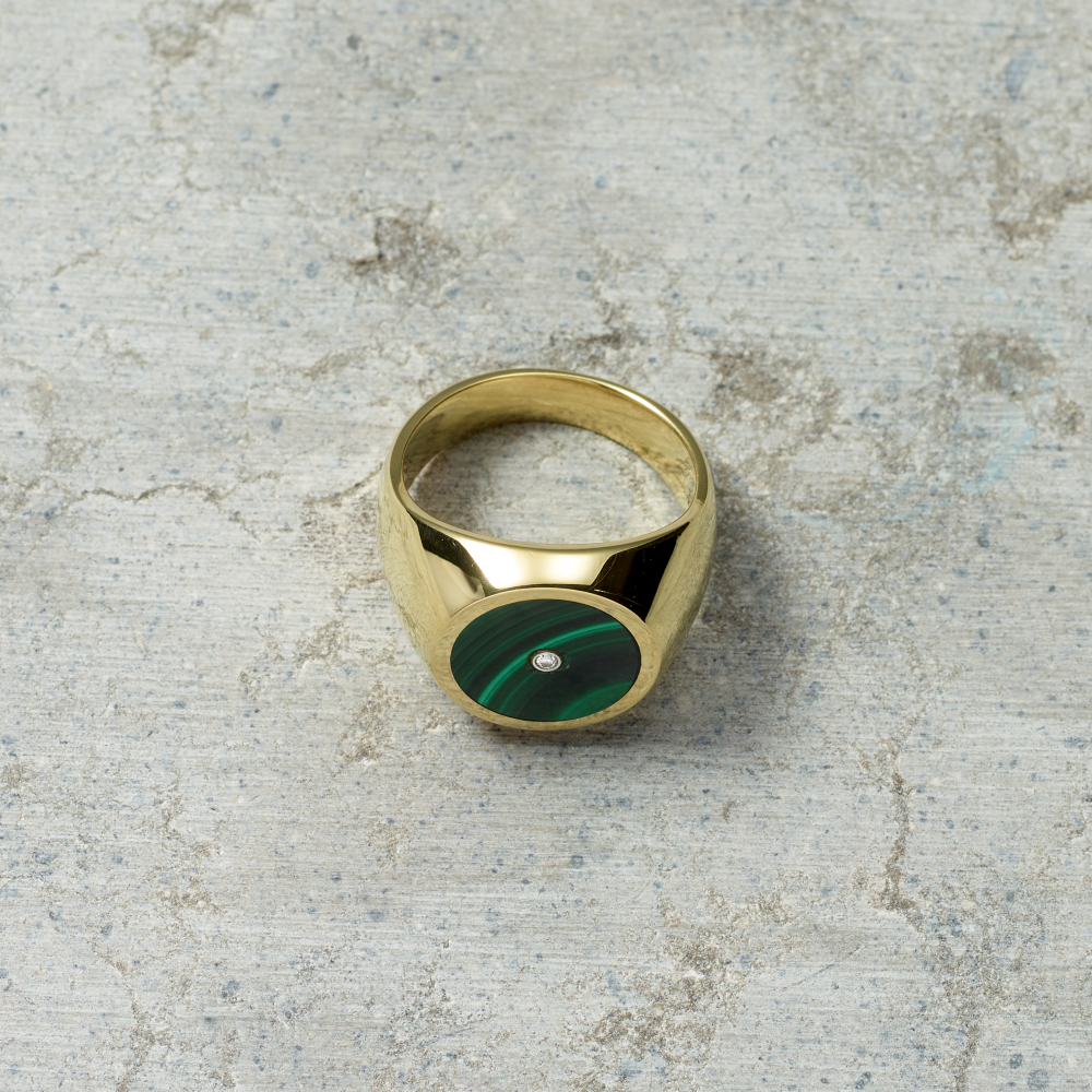 Gold ring with a green stone on a textured gray surface