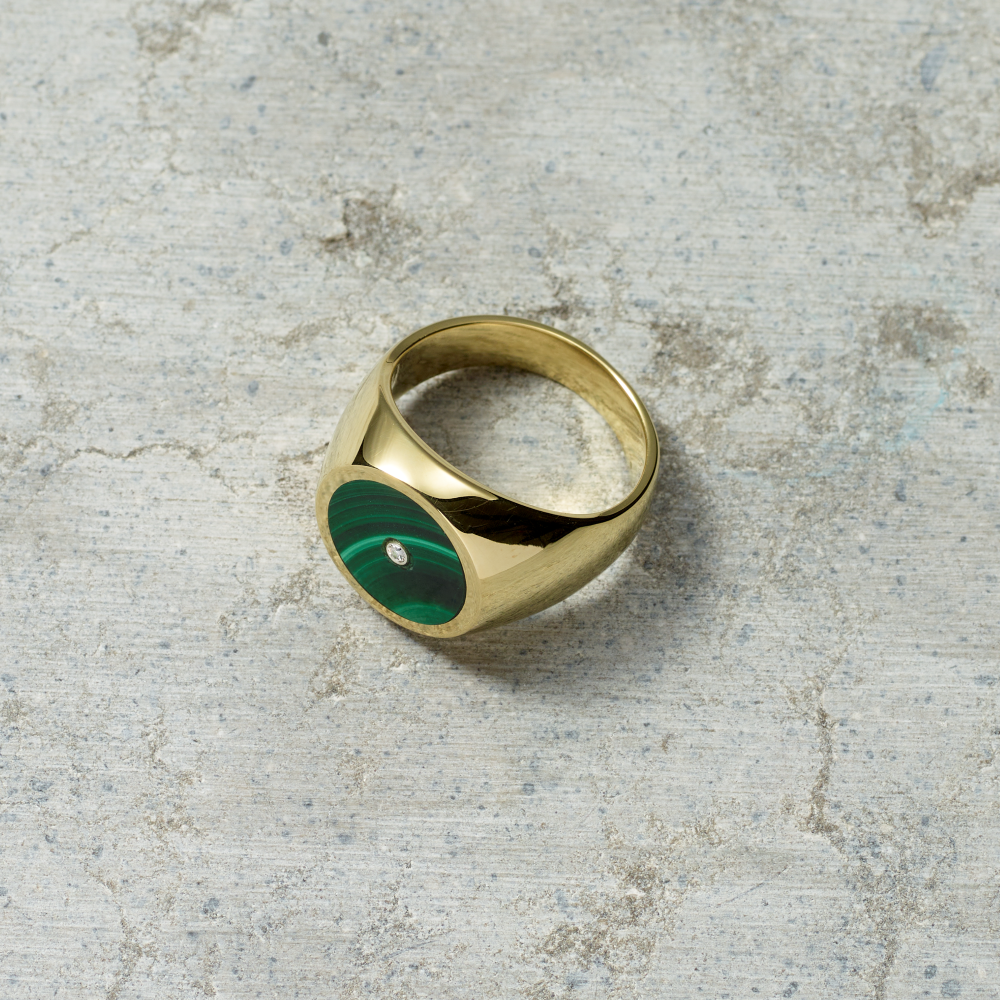 Gold ring with a green stone on a textured gray surface