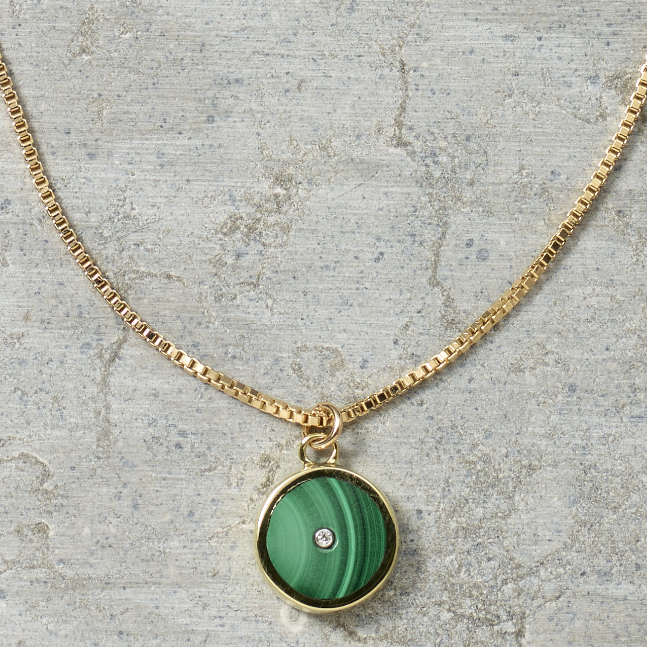 Gold necklace with a green pendant on a textured surface