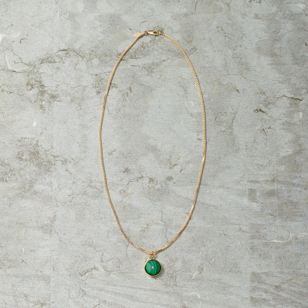 Gold necklace with a green pendant on a gray marble surface