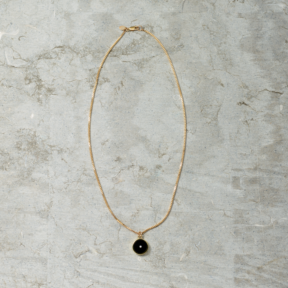Gold necklace with a black pendant on a gray marble surface