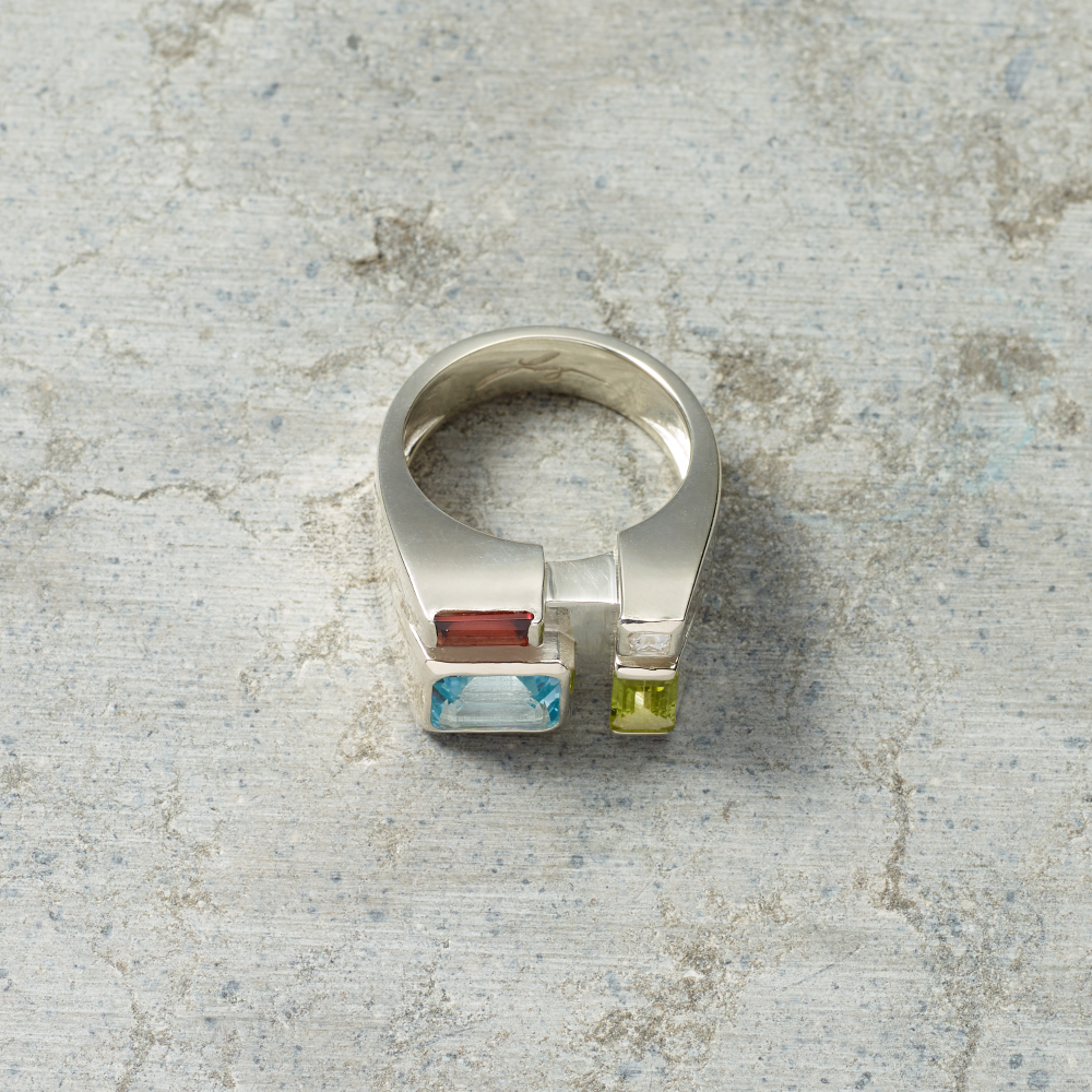 Silver ring with colorful gemstones on a textured surface