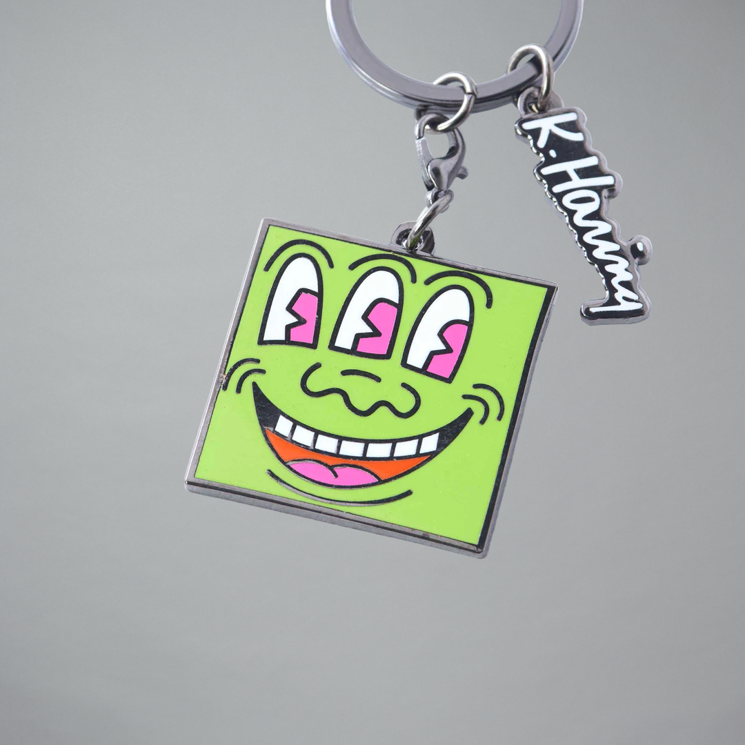 Keychain with a Keith Haring Three Eyed Monster design on a gray background