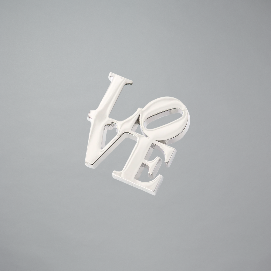 Robert Indiana Silver Love pin on a gray background