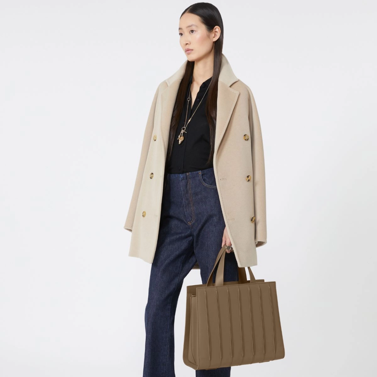 Model wearing a black coat and holding a camel bag on a white background