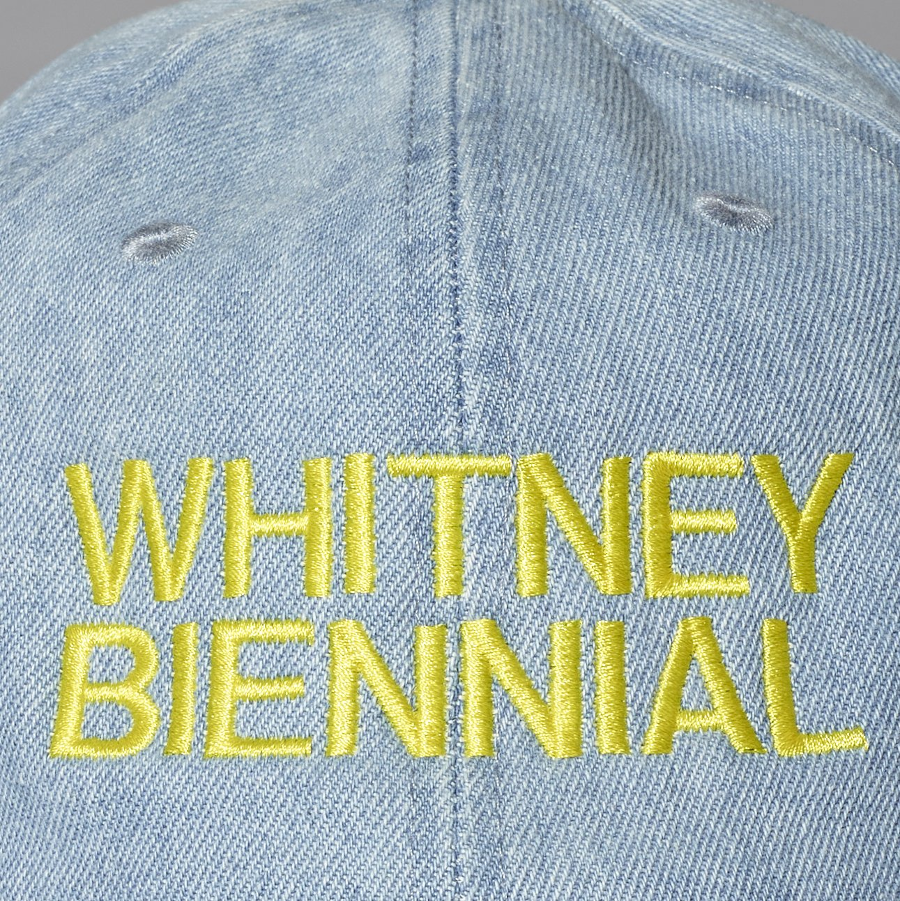 Light blue denim cap with 'WHITNEY BIENNIAL' embroidered in yellow.