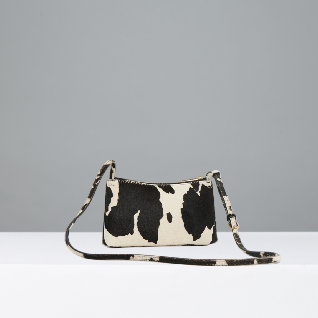 Black and white cow print handbag on a gray background