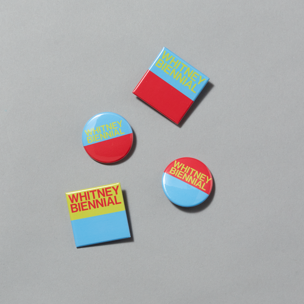 Set of four enamel pins in blue, red, and yellow colors displaying Whitney Biennial across each on a gray background