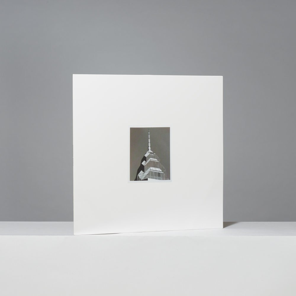 A square white vinyl records with a centered black-and-white photograph of a building spire, displayed upright on a white surface against a gray background.