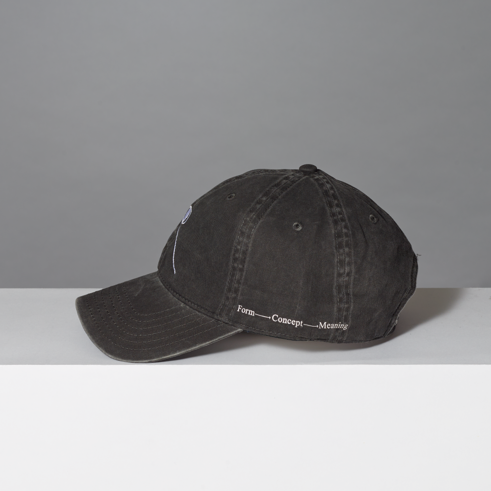 A washed black cotton baseball cap with white embroidered text reading 'Form Concept Meaning' on the side, displayed on a white surface against a gray background.