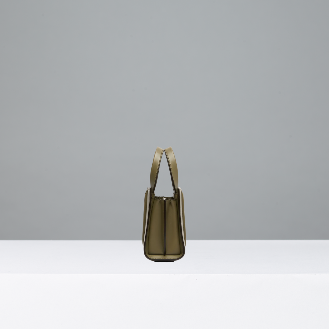 A structured leather handbag in a muted olive green color, shown from the back on a minimalist white platform against a solid gray background.