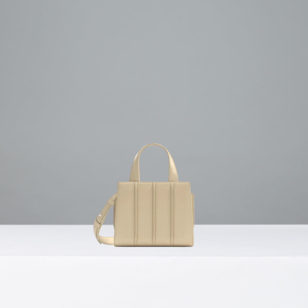 A structured beige leather handbag with dual top handles and a shoulder strap, displayed on a white surface against a gray background.