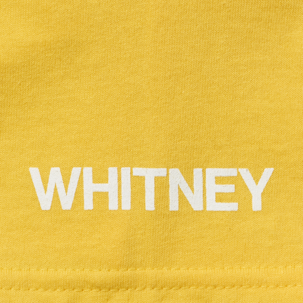 Whitney in white screen printed onto the sleeve of a yellow t-shirt