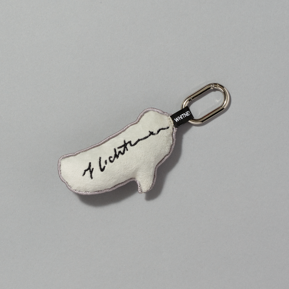 A small off-white plush keychain charm shaped like a quote bubble, featuring Roy Lichtenstein's signature against a gray background