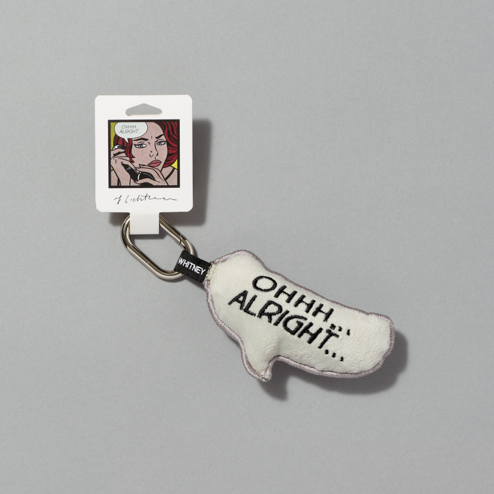 A small off-white plush keychain charm shaped like a quote bubble, featuring the text Ohhh... Alright... inspired by Roy Lichtenstein's work of the same name attached to a white tag with a depiction of the artwork