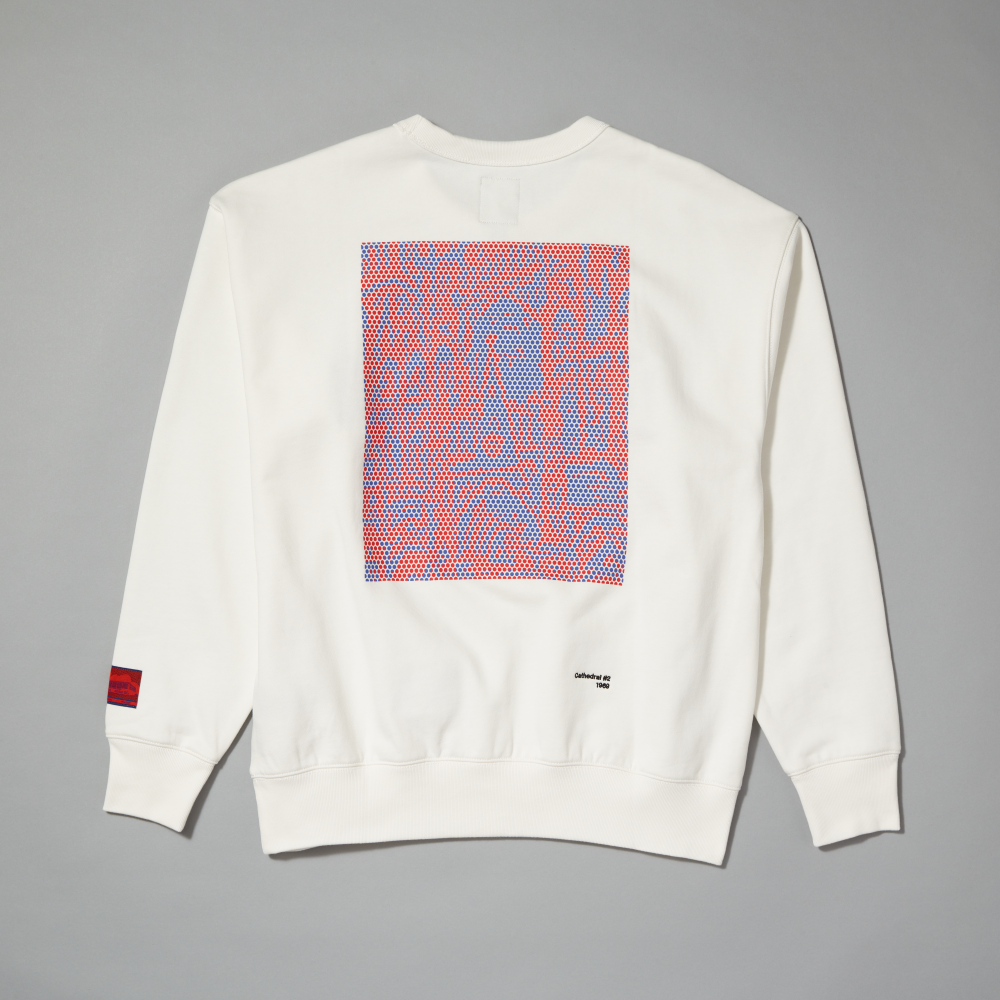 An off-white crewneck sweatshirt shown from the back, featuring a large square graphic print inspired by Roy Lichtenstein's work Cathedral #2 with a red and blue geometric pattern. A small red woven label is visible on the left sleeve cuff, laid against a gray background