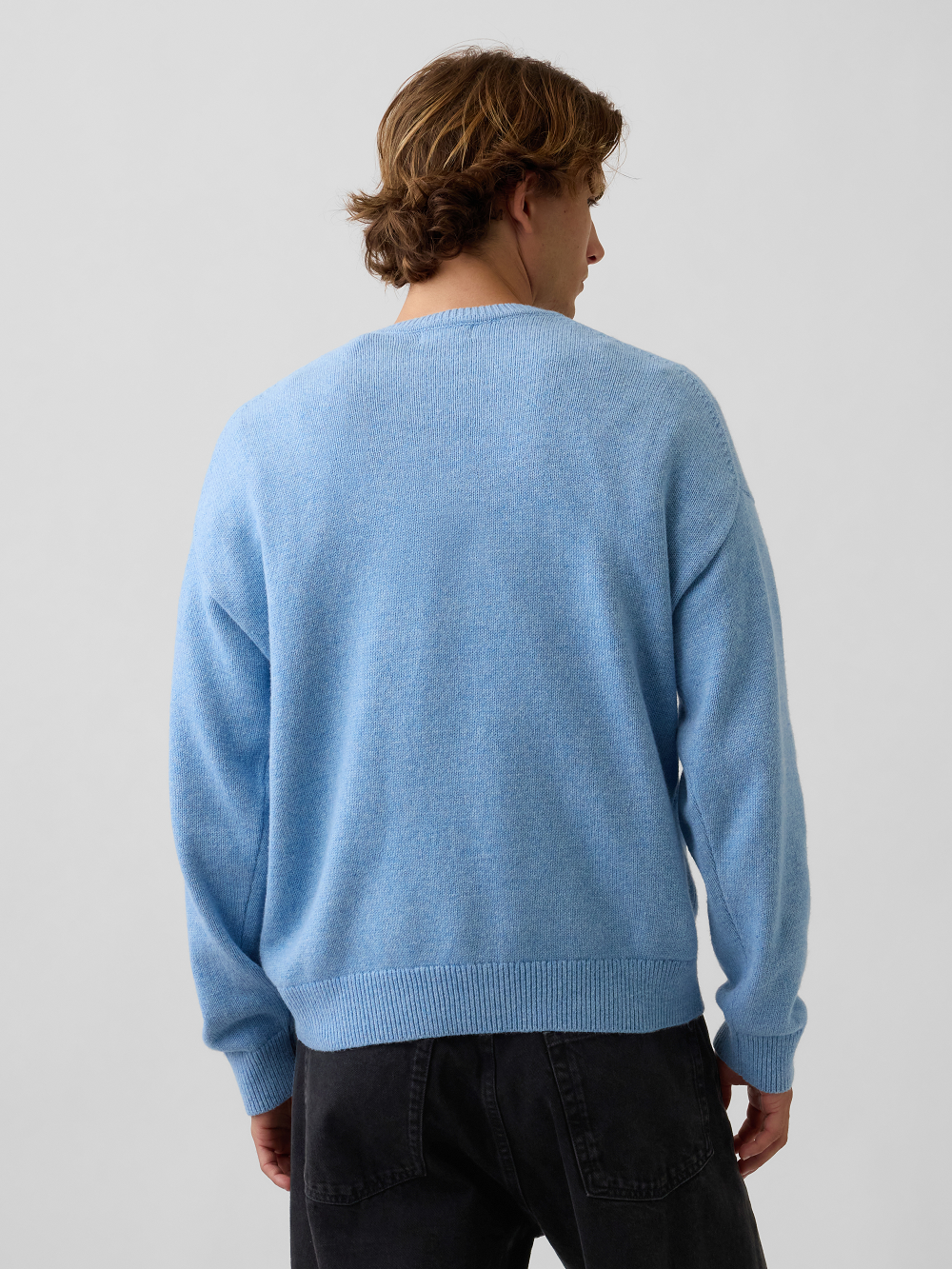 A model wearing a light blue crewneck sweater paired with black pants, against a light gray studio background