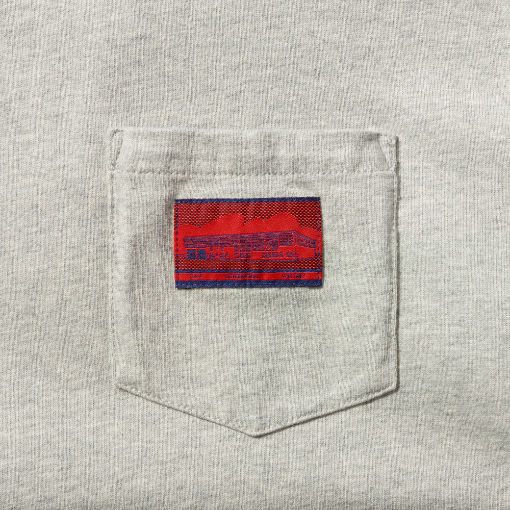 Close-up of a light heather gray fabric pocket with a red and blue woven label featuring Roy Lichtenstein's work Real Estate and the text GAP, LICHTENSTEIN and WHITNEY in the center