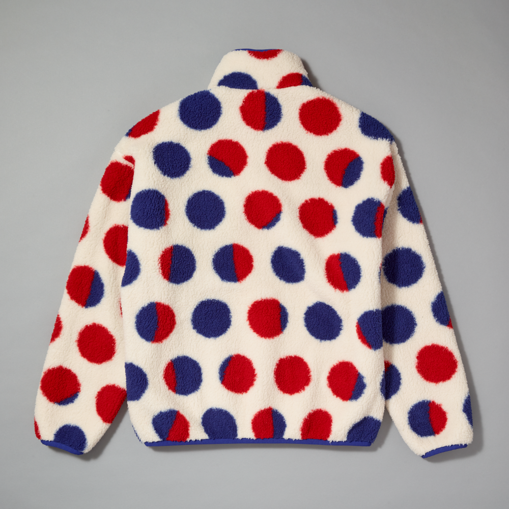 A fleece pullover sherpa with a red, white, and blue polka dot pattern inspired by Roy Lichtenstein's work Cathedral #2, shown from the back on a neutral gray background