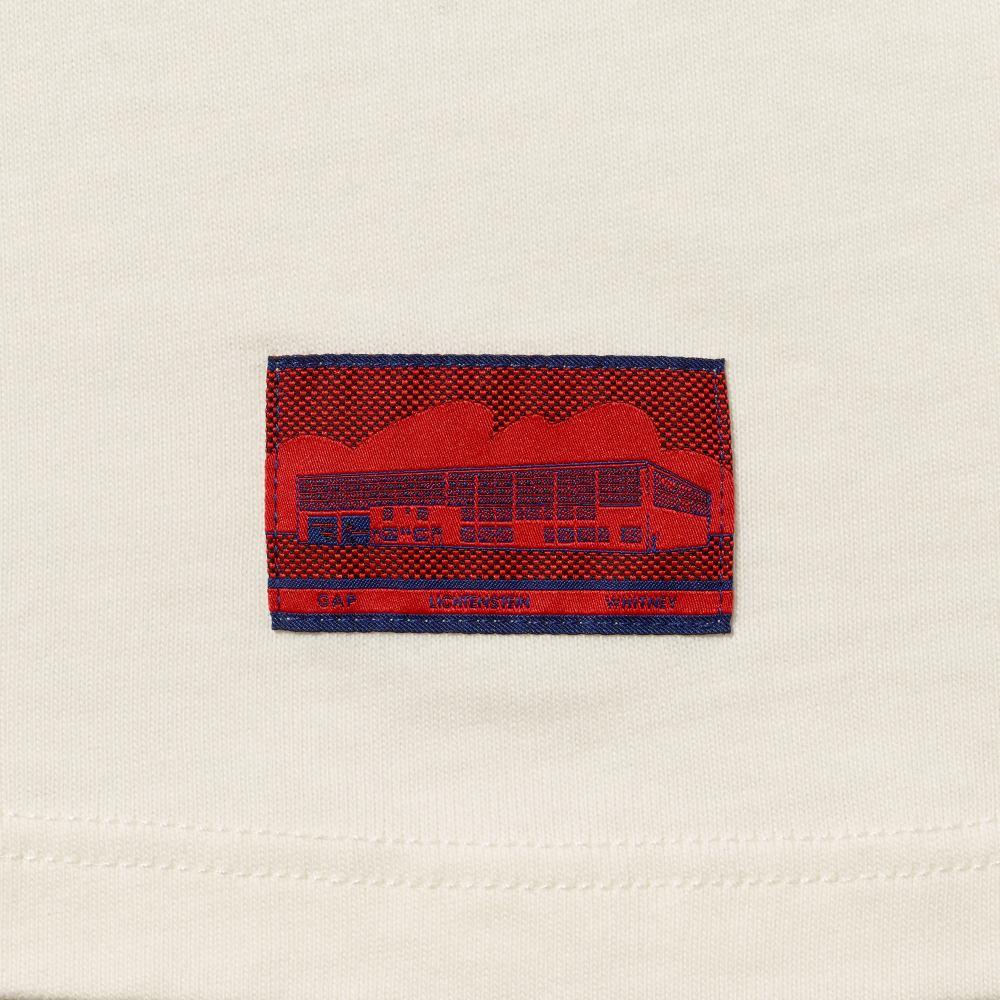 Close-up of an off-white garment with a red and blue woven label featuring Roy Lichtenstein's work Real Estate and the text GAP, LICHTENSTEIN and WHITNEY