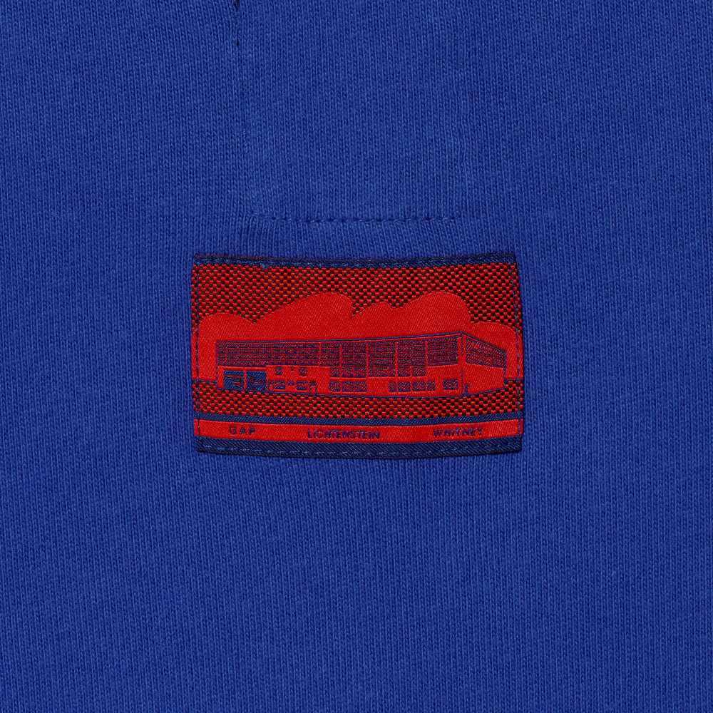 Close-up of a blue garment with a red and blue woven label featuring Roy Lichtenstein's work Real Estate and the text GAP, LICHTENSTEIN and WHITNEY