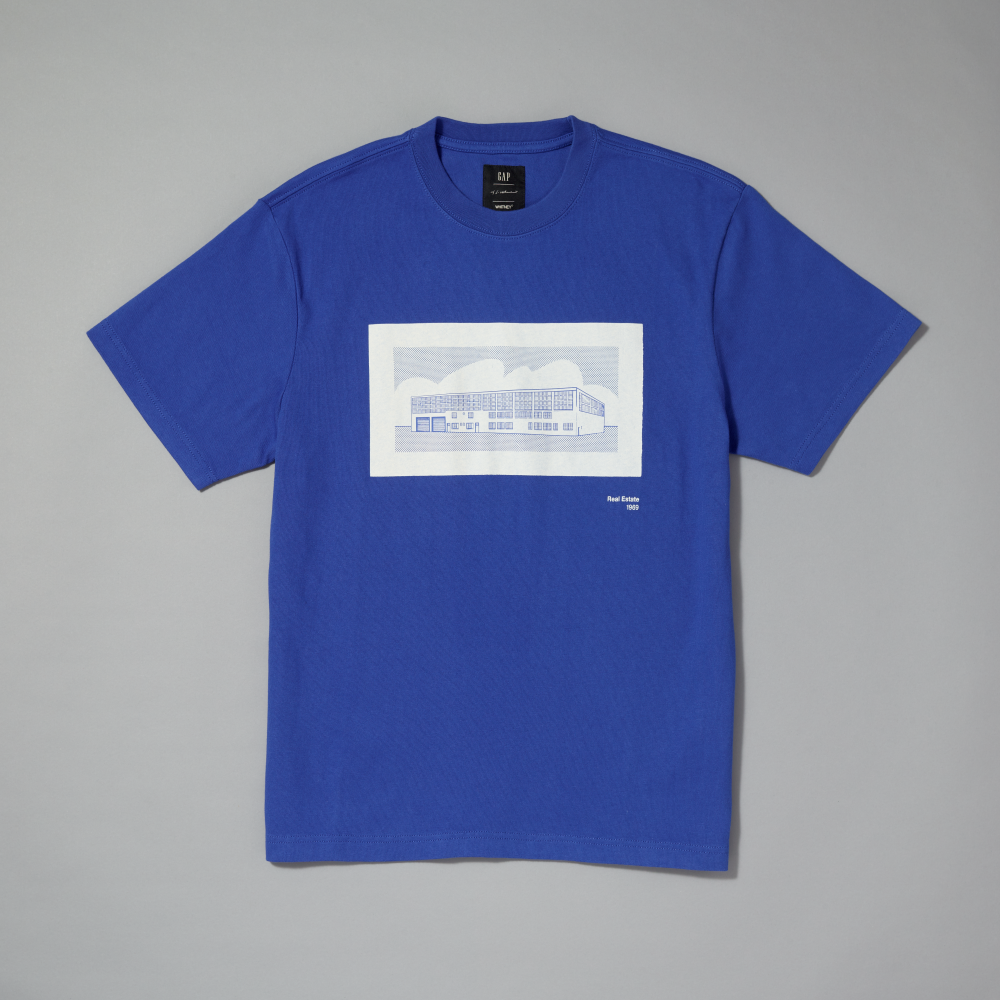 A royal blue short-sleeve crewneck t-shirt with a graphic print inspired by Roy Lichtenstein's work Real Estate on the chest laid flat on a neutral gray background