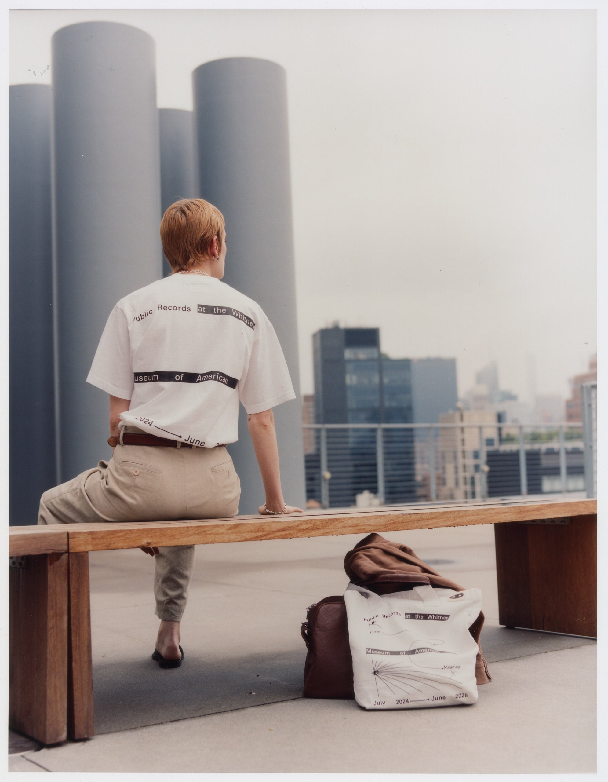 Model wearing 100% cotton white t-shirt featuring a graphic in black by Public Records with the 100% white canvas tote bag also by Public Records on the floor