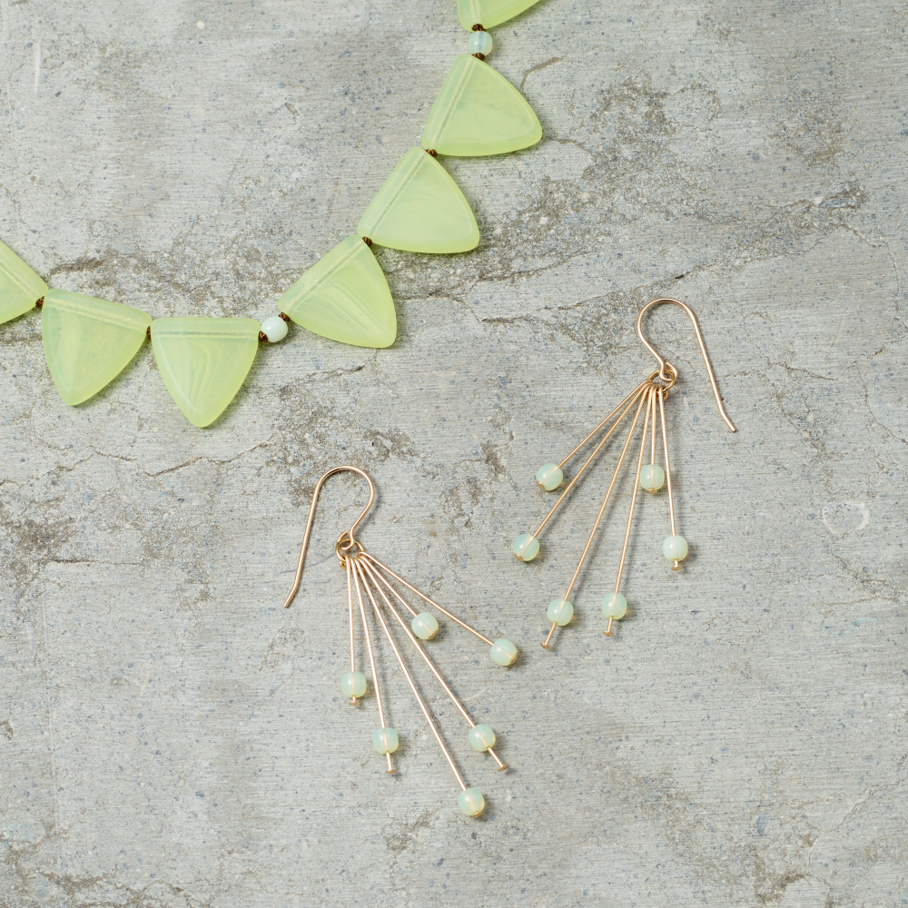 Gold earrings with green beads and necklace on a textured surface