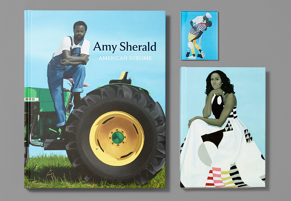 Assortment of products from the Amy Sherald: American Sublime exhibition, including the exhibition catalogue, magnet, and journal on a grey background.